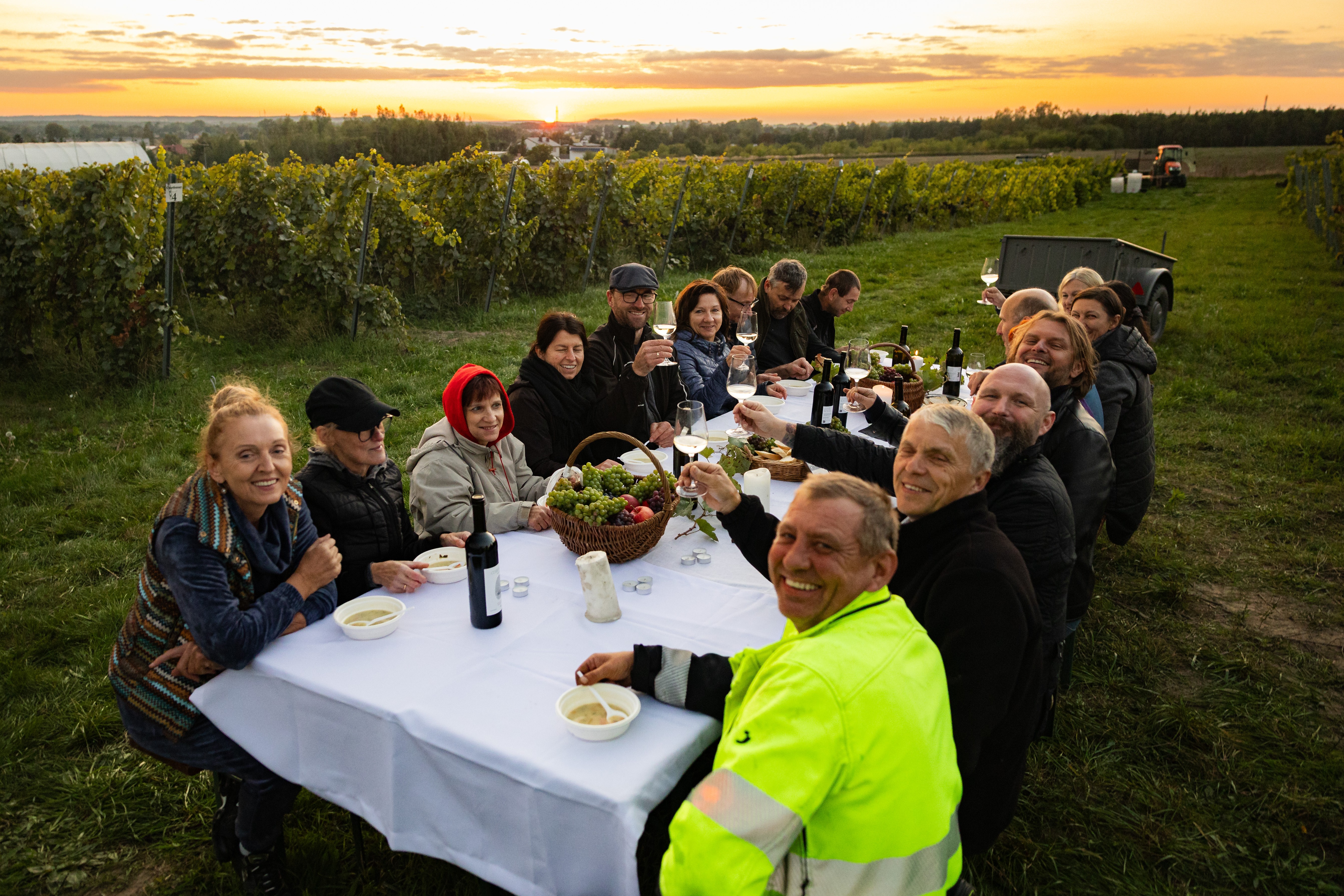 Grupa osób siedzi przy stole po środku winorośli w Winnicy Warto
